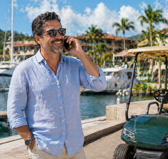 middle aged Hispanic man talking on phone at marina in Costa Rica with golf cart and yachts enjoying relaxed lifestyle
